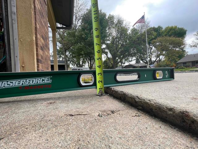 Measuring a severe concrete slab drop next to a brick foundation using a level tool in Blaine, MN.