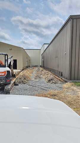 active-drainage-trench-excavation-thorp-wi An active excavation site in Thorp, WI showing a compact excavator digging trenches between industrial buildings for a commercial waterproofing project.
