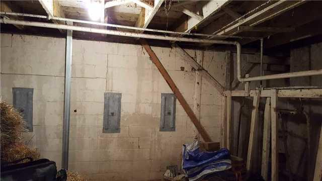 A completed foundation repair project inside a barn utility space in Fall Creek, WI, showing three heavy steel GeoLock anchor plates and one vertical PowerBrace I-beam column installed against a cracked concrete block wall.