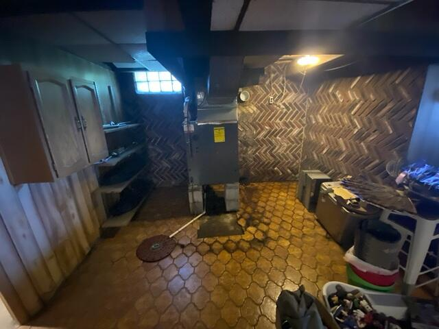 A damp basement room with patterned gold hexagonal floor tiles showing heavy water damage and pooling moisture around a central furnace in Carlton, MN.