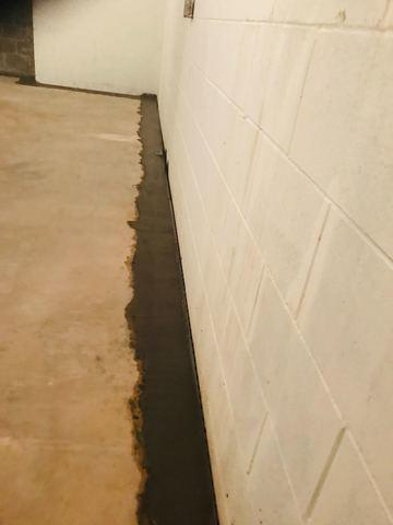 A close-up view of a clean concrete block basement wall showing a freshly poured concrete perimeter trench patch over an installed WaterGuard interior drainage system in Hager City, WI.
