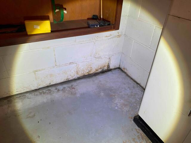 A dark basement corner illuminated by a flashlight beam showing damp concrete block foundation walls and moisture staining in Stone Lake, WI before professional repair.
