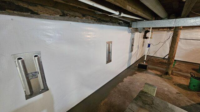 Wide-angle view of a waterproofed basement featuring bright white CleanSpace encapsulated walls, multiple heavy-duty steel GeoLock anchor plates, and fresh concrete floor perimeters in Marengo, WI.
