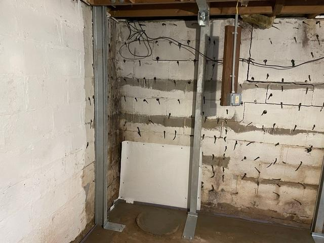 Heavy-duty zinc-plated steel PowerBrace columns installed along a cracked concrete block foundation wall with a freshly poured concrete floor perimeter track in a Neillsville, WI basement.