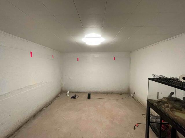 An empty white basement room in Ashland, WI featuring bright red tape markers placed along the walls to evaluate structural bowing before repair.