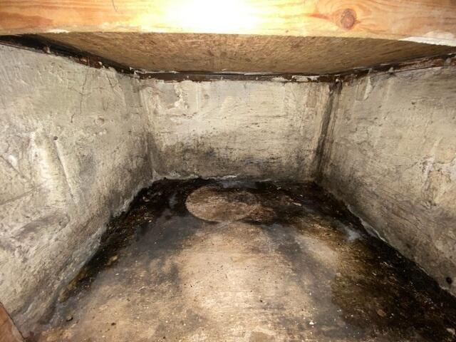 A raw, uninsulated concrete basement corner showing severe moisture staining and structural washout along the floor joint in Carlton, MN before repair.