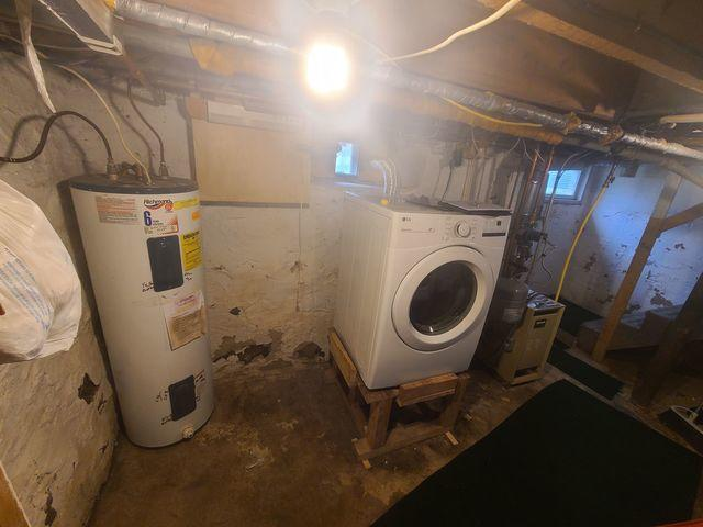 An unfinished basement utility area showing a washing machine on a wooden stand, water heater, and damp concrete walls in Baldwin, WI before repair.