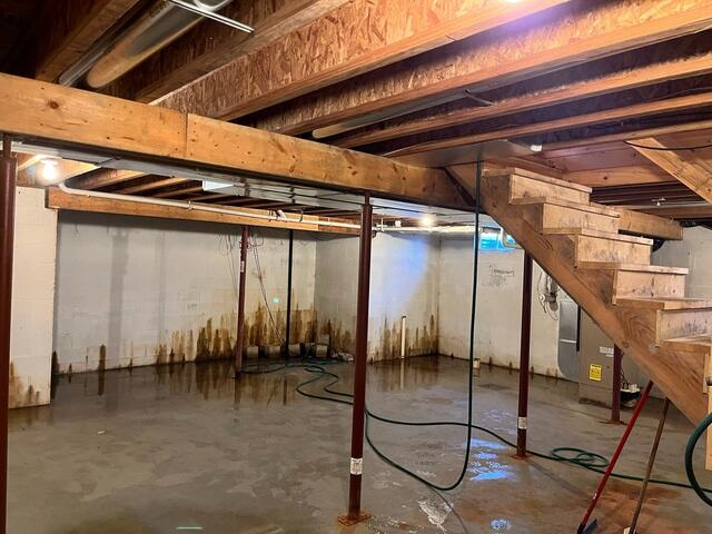 An old, open sump pump pit and dirty drainage hose surrounded by water-stained concrete block walls in Birchwood, WI.