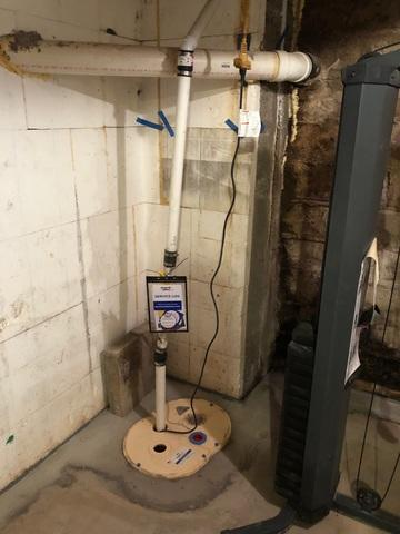 A newly installed heavy-duty sump pump system with clean PVC lines and an attached service log in a Chippewa Falls, WI basement.