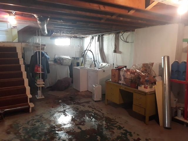 Severe standing water flooding a concrete basement floor near a washing machine and wooden staircase in a Cloquet, MN home before repair.