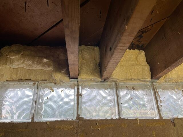 Close-up of spray foam insulation applied to the rim joist area above glass block windows in Cloquet, MN.
