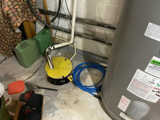 An old yellow-lidded sump pump pit located next to a water heater in a Cohasset, MN basement before a professional upgrade.