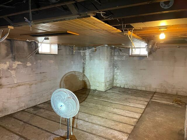 An unfinished and damp basement layout with bare block foundation walls and a floor fan before waterproofing in Conrath, WI.