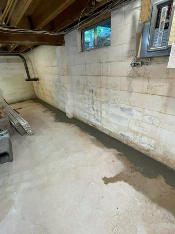 A freshly poured concrete border patch covering an installed sub-floor interior perimeter drainage system along a concrete block foundation wall in Cornucopia, WI.