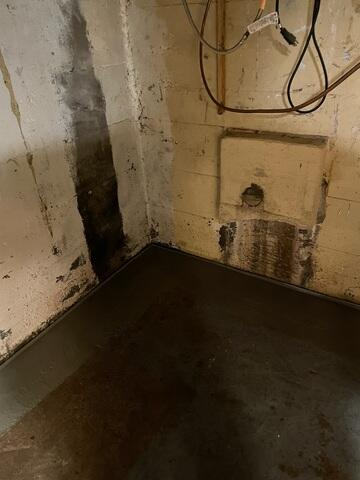 Dark water intrusion stains running down concrete block basement walls near a newly installed floor track in Gordon, WI.