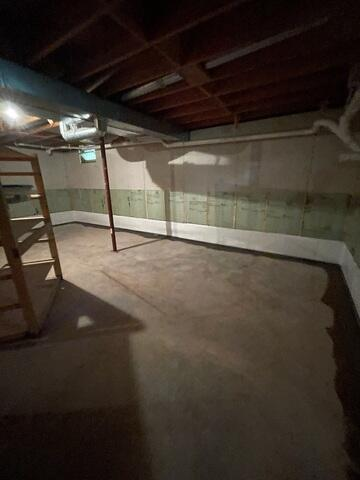 An expansive overview of a clean concrete basement floor showing a freshly poured perimeter trench patch along walls covered with white and green insulation panels in Hayward, WI.