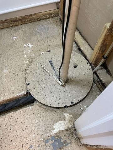 Close-up of a flush circular access lid assembly cleanly sealed into a concrete basement floor with a corrugated line in McGregor, MN.