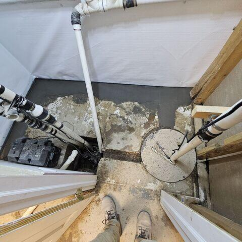 Top-down view of a technician's boots next to a freshly concreted sub-floor perimeter drainage track and sealed sump pump covers in McGregor, MN.