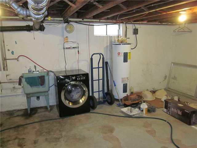 An unfinished utility basement area showing a washing machine, water heater, and laundry tub in Medford, WI before professional repair.
