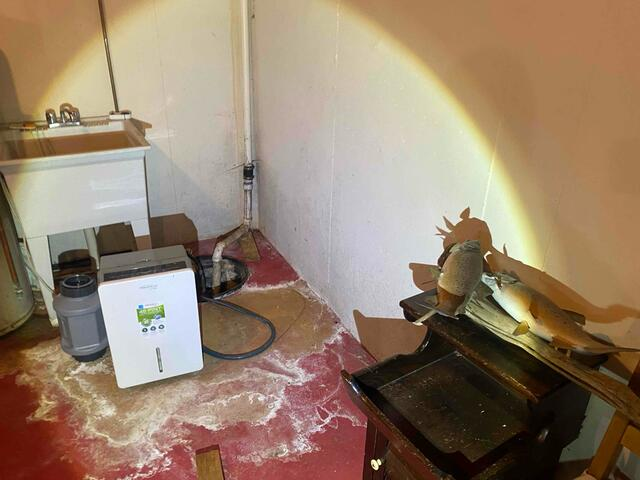 Damp red-painted basement floor showing heavy moisture stains near an open sump pit and white utility sink in South Range, WI before repairs.