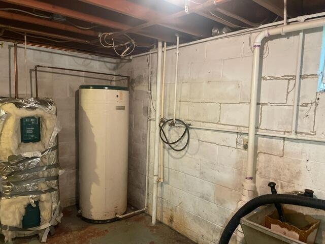 A raw concrete block foundation wall showing cracks and water stains next to utility tanks in a South Range, WI basement before professional repair.