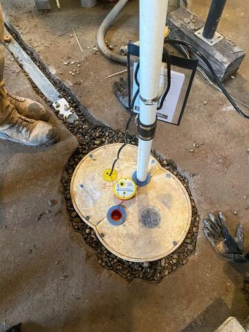 A heavy-duty TripleSafe sump pump basin embedded in a concrete basement floor and surrounded by clean drainage stones in Washburn, WI.