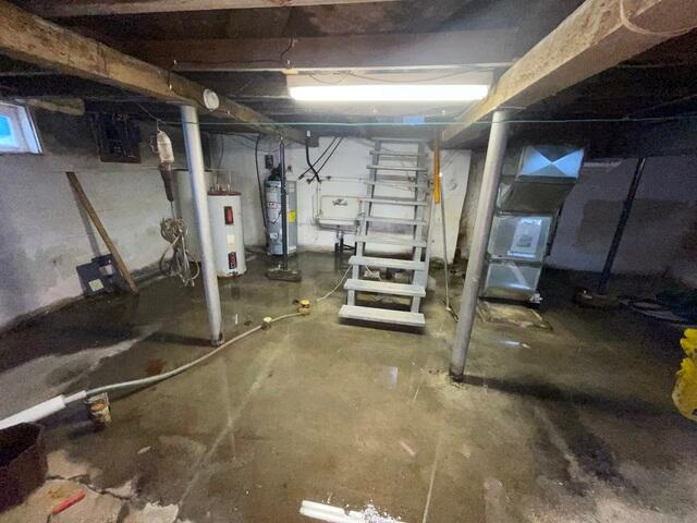 Severe standing water flooding a concrete basement floor near utilities and a wooden staircase in Washburn, WI before a professional repair.