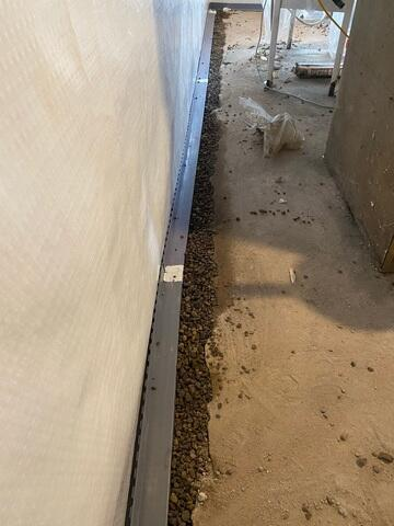 WaterGuard interior perimeter drainage track being installed in a stone-filled floor trench next to a white wall liner in Washburn, WI.