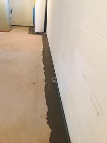 An immaculate basement floor showing a freshly poured concrete trench patch covering an installed WaterGuard interior drainage system along a clean white block wall in Webster, WI.