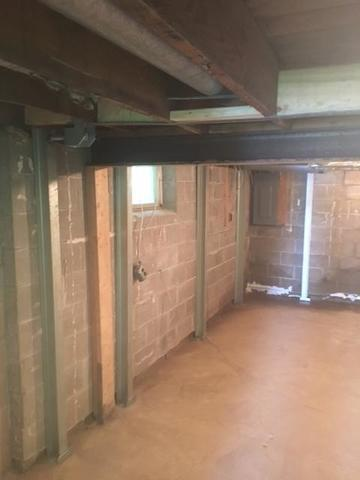 An interior basement view of a cabin in Saint Croix Falls, WI featuring several vertical steel PowerBrace support columns cleanly reinforcing a concrete block foundation wall beneath wooden floor joists.
