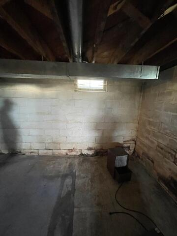 An unfinished concrete block basement wall showing horizontal mortar cracks and a brown dehumidifier on the concrete floor in Eau Claire, WI before repair.