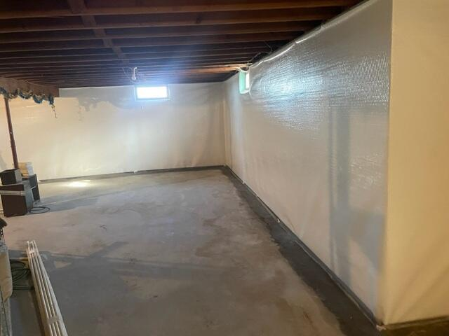 A wide view of a clean, empty basement featuring bright white vapor barrier liners wrapped smoothly across the entire foundation wall perimeter in Eau Claire, WI.