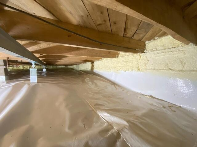 A close-up view inside a newly encapsulated crawl space in Mercer, WI showing a white vapor barrier meeting yellow spray foam insulation along the foundation header.