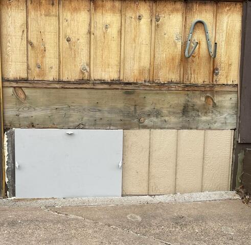A finalized exterior view of a completed insulated crawl space access hatch surrounded by clean tan vertical siding panels in Jim Falls, WI.
