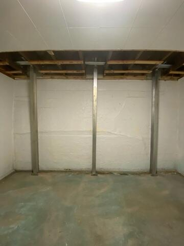 completed-powerbrace-steel-ibeam-wall-support-ashland-wi A completed foundation repair project in Ashland, WI showing three vertical steel PowerBrace support columns tightly installed to stabilize a white basement wall.