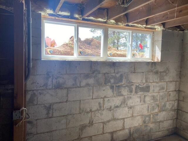 A beautifully installed white vinyl sliding egress window admitting bright daylight into a concrete block basement room in Wrenshall, MN.