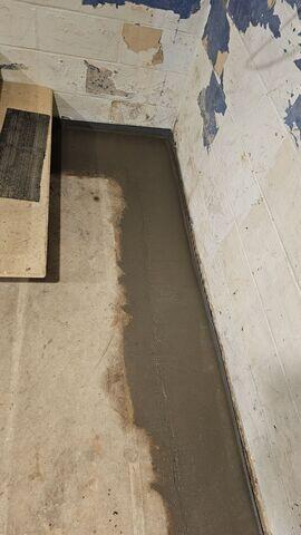 An immaculate view looking down a concrete block basement wall corner in Remer, MN, featuring a freshly poured smooth concrete track sealing a WaterGuard drainage system.
