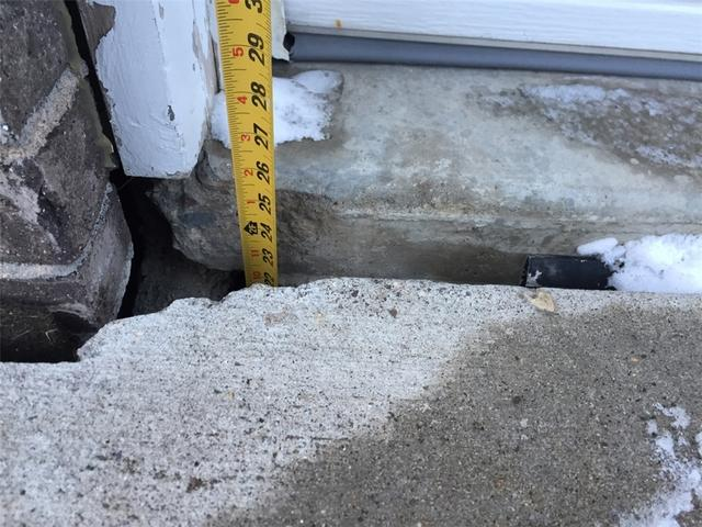 Using a tape measure to check the severe multi-inch drop and separation of a sunken concrete garage apron in Roberts WI before repair