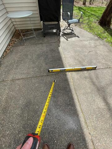 Measuring a sunken concrete patio slab with a level and tape measure before repair in Anoka, MN.
