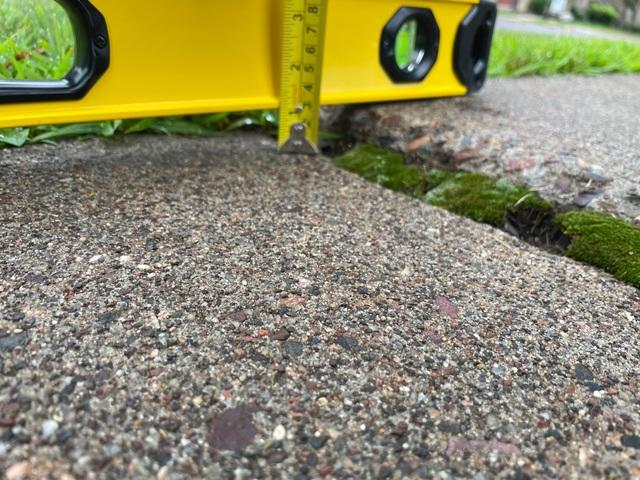 Uneven concrete sidewalk slab in Colfax WI being measured with a level tool before concrete repair service
