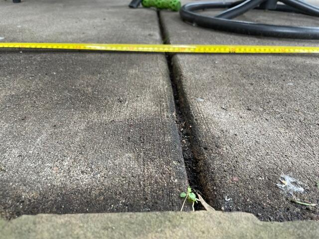 concrete-repair-duluth-mn-before-joint Close-up of a deep, uneven concrete joint gap being measured with a tape measure tool in Duluth, MN.