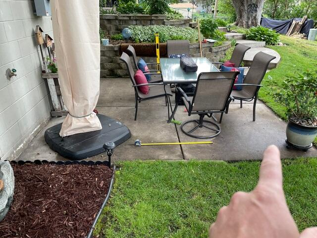 Sunken concrete patio slab under an outdoor dining set showing water pitch issues in Duluth, MN.