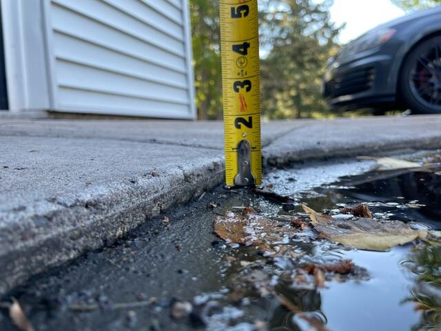 Measuring a three quarter inch concrete lip on a driveway transition with a tape measure in Esko MN