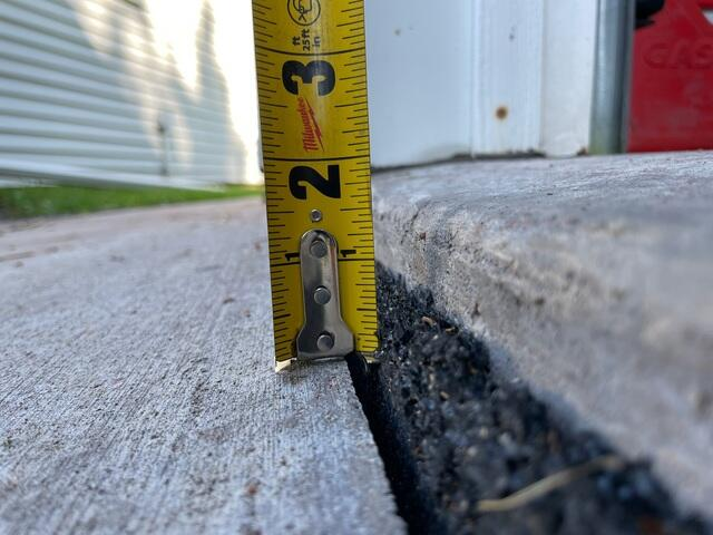 Measuring a two inch drop on a concrete garage apron with a tape measure before repair in Esko MN