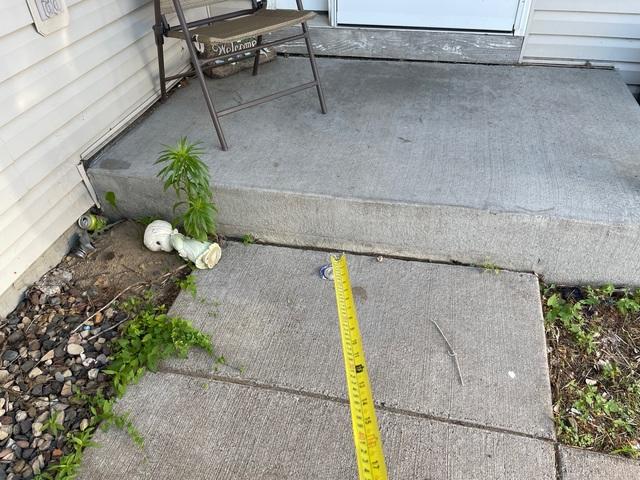 Measuring a sunken concrete sidewalk slab creating an uneven lip before repair in Hammond, WI.