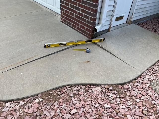 Measuring a cracked and uneven concrete driveway apron with a level tool before repair in New Richmond, WI.