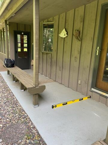 Sunken concrete walkway along a home porch showing a yellow level tool before concrete repair in Osceola WI