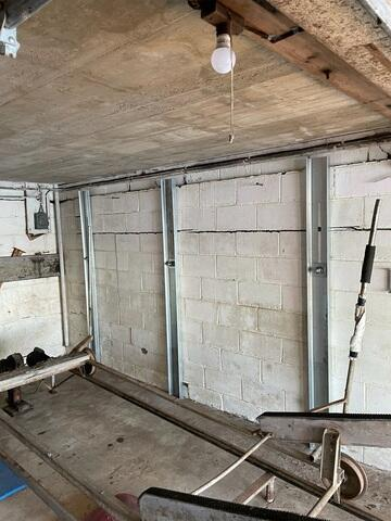 A long view of a boat house interior showing three heavy-duty vertical steel wall supports mounted over a cracked concrete block foundation wall in Amery, WI.
