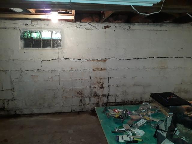 A raw concrete block basement foundation wall showing a severe horizontal crack across mortar joints and heavy moisture staining near the floor in Cloquet, MN before repair.