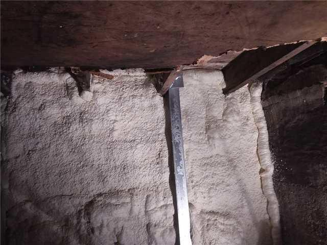 Polyurethane spray foam insulation applied along a crawl space wall behind a PowerBrace steel bracing beam in Cloquet Minnesota